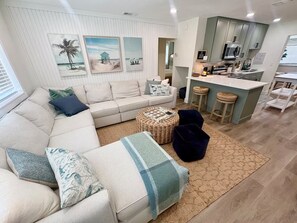 Uma sala de estar moderna com sofá, um banquinho e uma área de cozinha com banquetas.