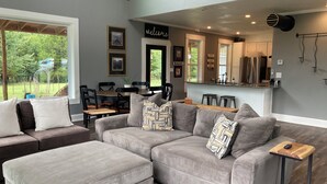 A modern living room with a grey sectional sofa, a dining area with a wooden table and chairs, and a kitchen with a stainless steel refrigerator. - 4 bed 3.5 bath on 5 acres 5 minutes to Walmart supercenter and 6 minutes to OSU. (Stillwater)