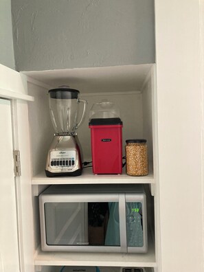 Une étagère de cuisine avec un mixeur, un appareil de couleur rouge et un récipient rempli de céréales.