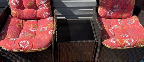 Two wicker chairs with floral cushions, a black table, and a multicolored striped rug.