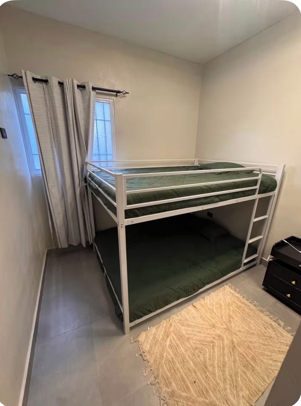 A bunk bed in a room with a window, curtains, and a rug.