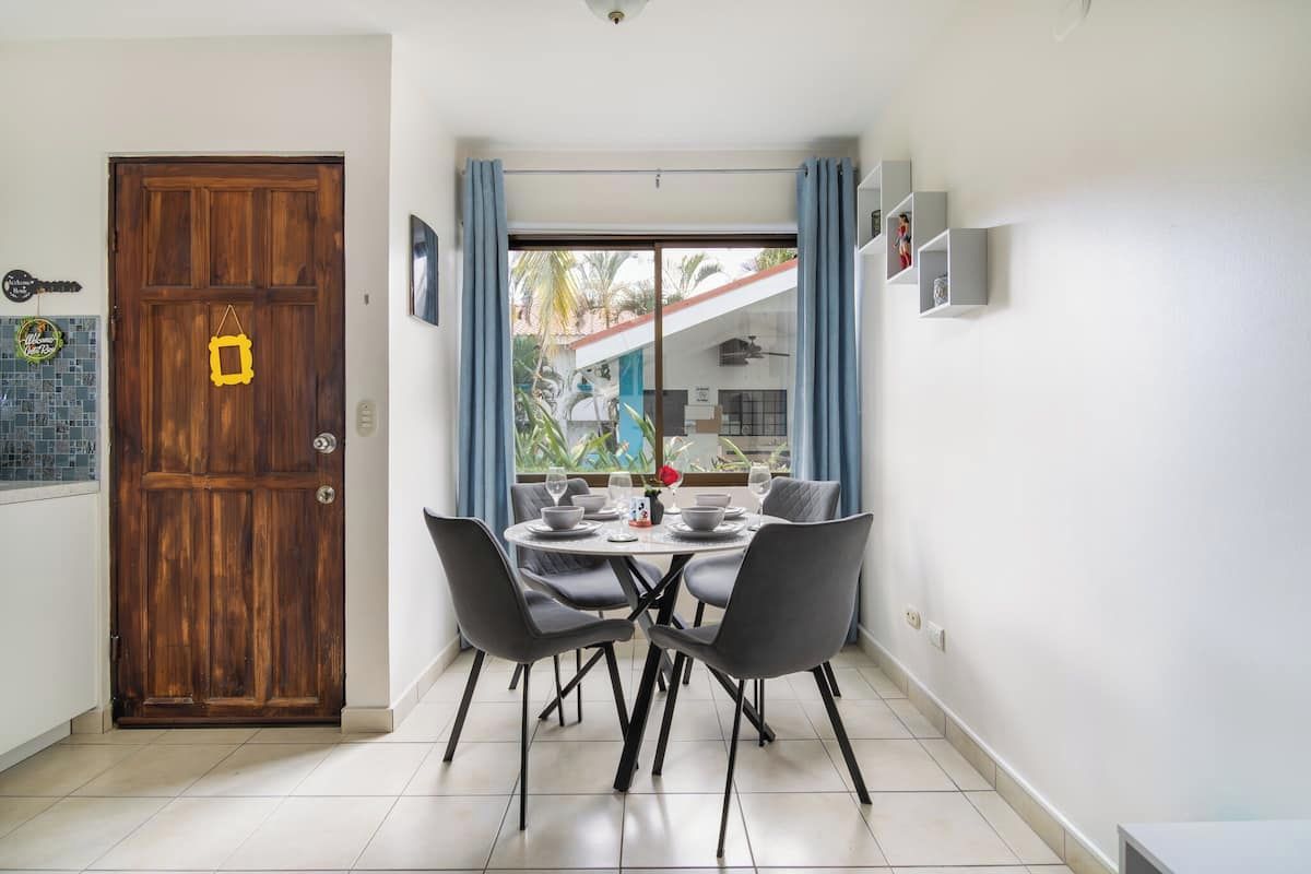 Un coin repas avec une porte en bois, une table à manger avec des chaises, et une vue sur l’extérieur à travers une porte vitrée.