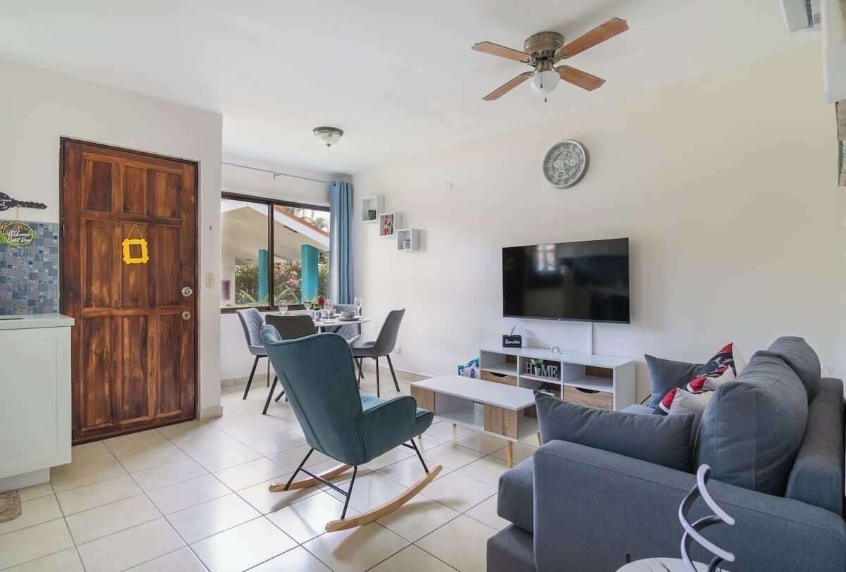 A modern living room with a television, sofa, and a dining area with chairs.