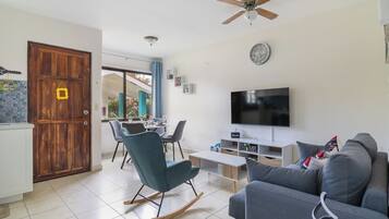 A modern living room with a television, sofa, and a dining area with chairs.