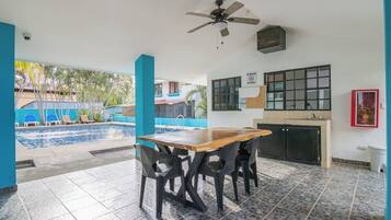 An outdoor dining area with a pool, a ceiling fan, and a kitchen area.