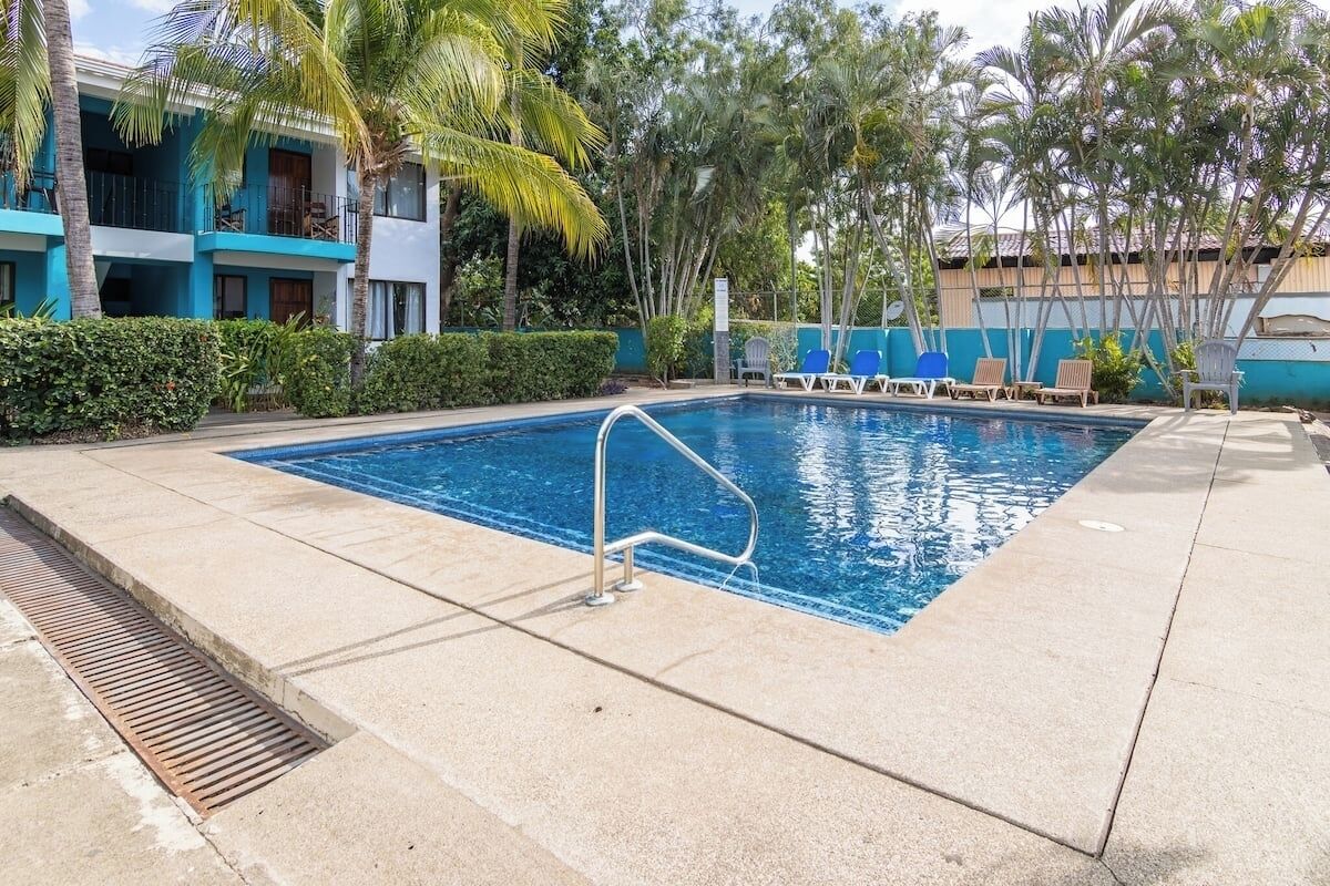 A swimming pool with a metal ladder, surrounded by lounge chairs and palm trees.