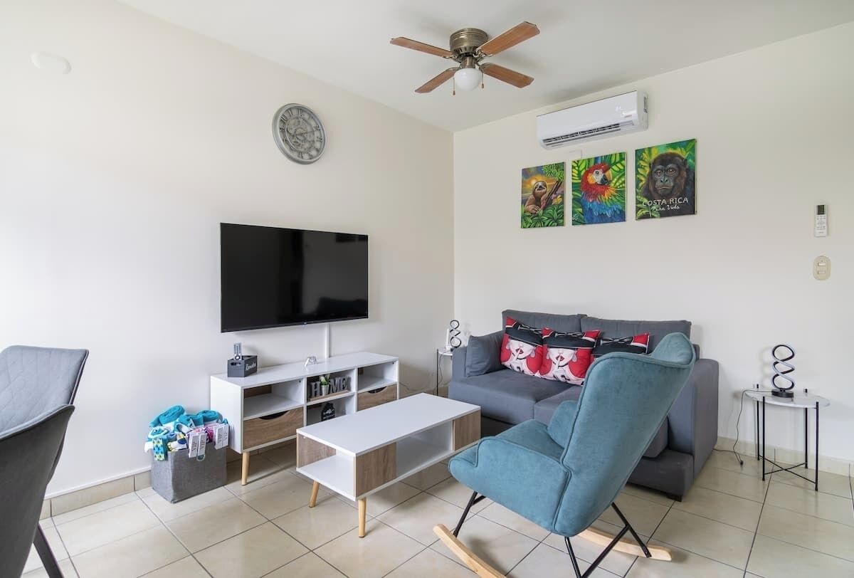 Un salon moderne doté d’un téléviseur à écran plat, d’un ventilateur de plafond, d’un canapé, d’un fauteuil bleu et d’œuvres d’art accrochées au mur.
