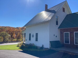 A two-story house with a metal roof, a front porch, and a driveway. - Family-Friendly Vermont Retreat Near Mount Snow | VAST Trail Access & Walk to Downtown (Wilmington)