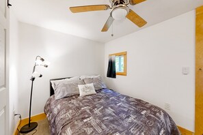 Ein Schlafzimmer mit einem Bett, einem Deckenventilator, einem Fenster mit Vorhang und einer Stehlampe.