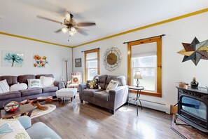 A cozy living room with a fireplace, a ceiling fan, and a star decoration on the wall. - Family-Friendly Vermont Retreat Near Mount Snow | VAST Trail Access & Walk to Downtown (Wilmington)
