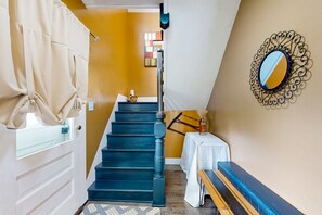 Eine Treppe mit dunklen Stufen führt zu einer Zwischenebene, dort steht ein weißer Tisch mit einer Vase und ein dekorativer Spiegel an der Wand.