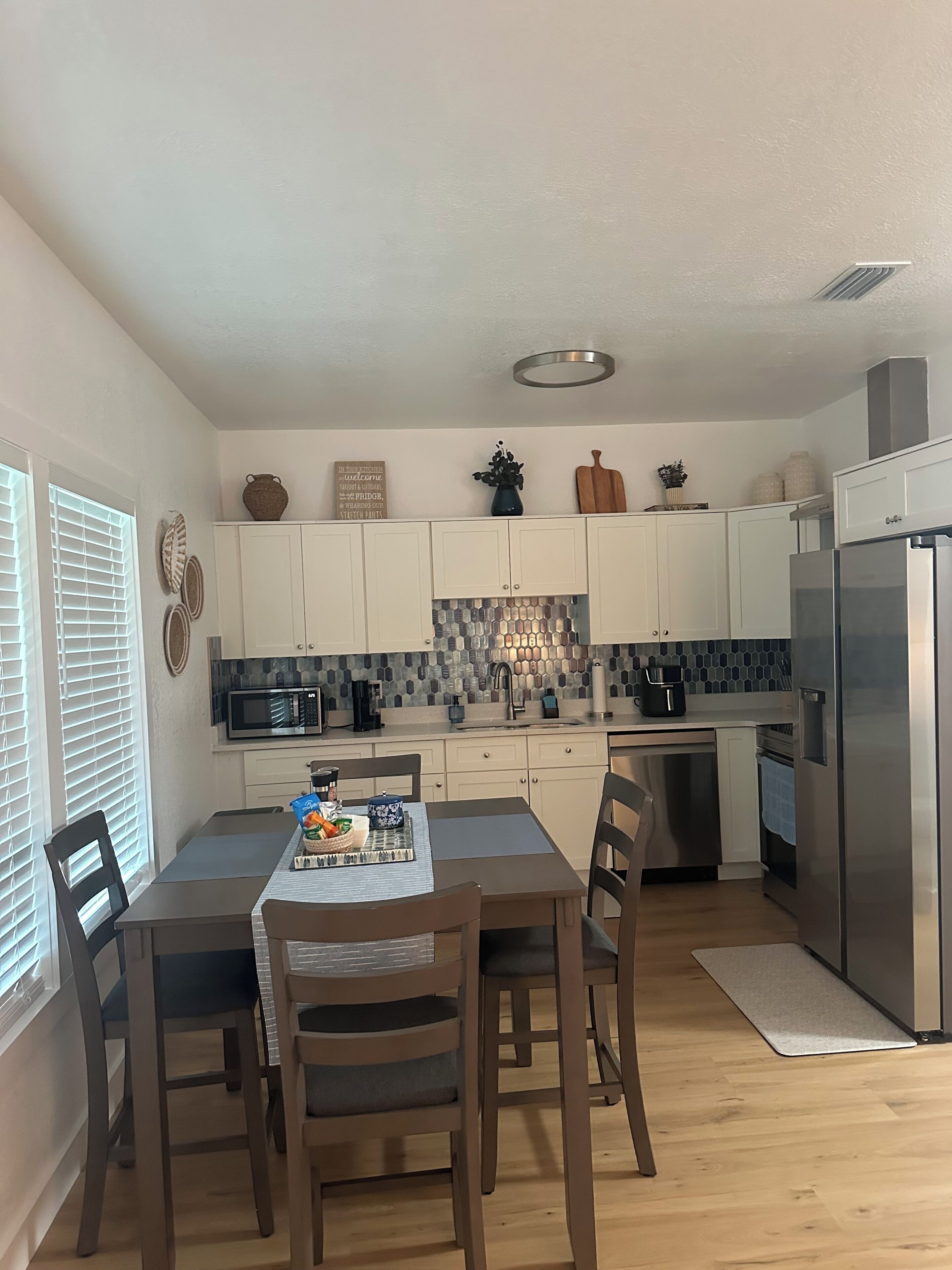 A modern kitchen with white cabinets, a stainless steel refrigerator, and a dining area with a table and chairs.