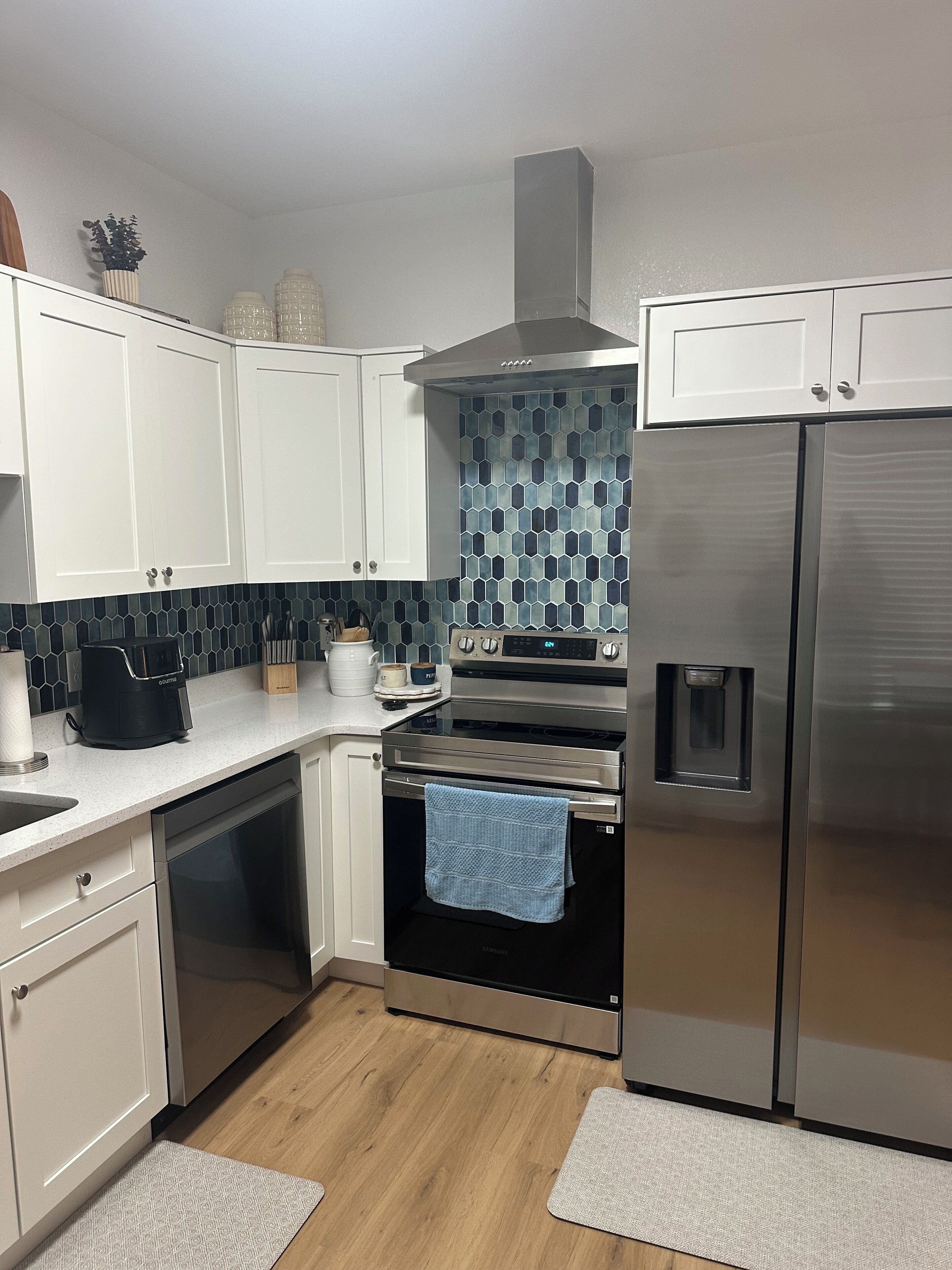 Una cocina moderna con armarios blancos, una campana de acero inoxidable, horno integrado y un refrigerador.