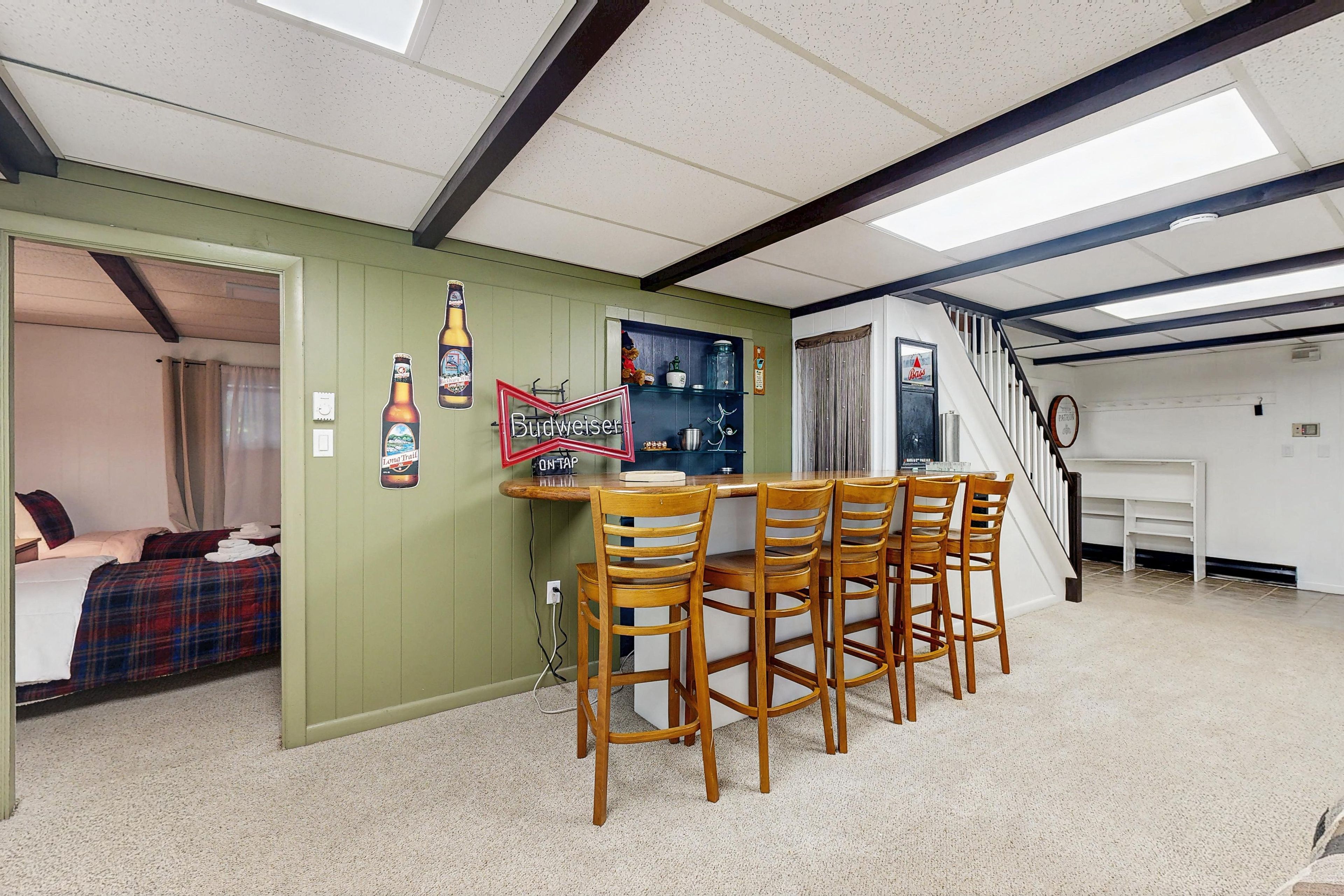 A room with a dining area featuring a wooden table and chairs, a kitchen area with a stove and cabinets, and a bedroom with a bed and curtains.