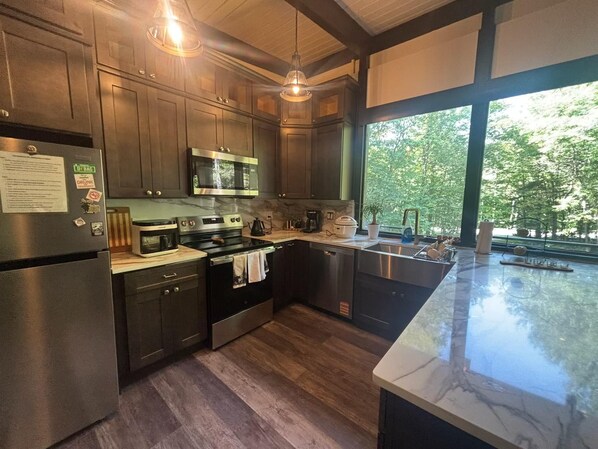 Une cuisine moderne dotée d’appareils électroménagers en acier inoxydable, de meubles en bois et d’une grande fenêtre offrant une vue sur les arbres.