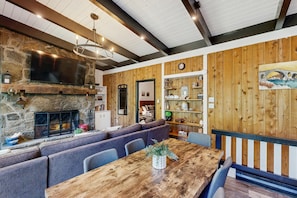 A cozy interior with a stone fireplace, wooden panel walls, a dining area with a wooden table, and a seating arrangement. - Mountain-view Wilmington home with well-appointed kitchen near Mount Snow (Wilmington)
