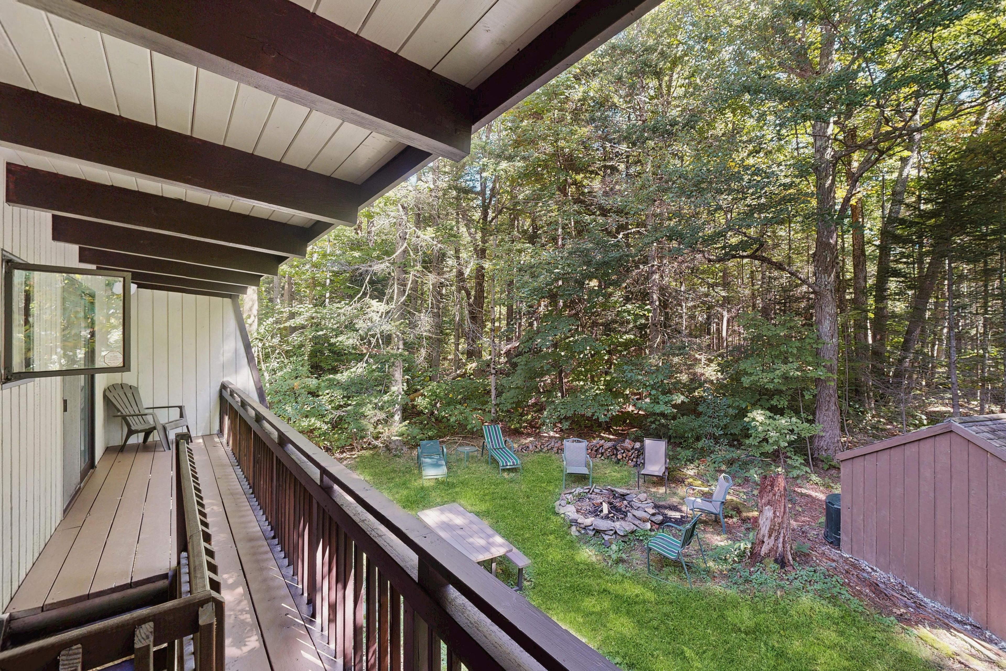 Une terrasse couverte avec vue sur une zone boisée, des sièges d’extérieur et un foyer.