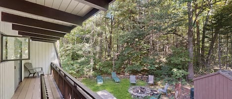 Une terrasse couverte avec vue sur une zone boisée, des sièges d’extérieur et un foyer.