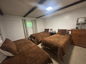 Une chambre avec deux lits simples, une commode, une table de chevet et une fenêtre avec des rideaux.