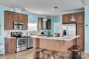 A modern kitchen with wooden cabinets, stainless steel appliances, a marble countertop, and bar stools. - Canal Home: Private Pool, Hot Tub, Dock and Pilings (Marathon)