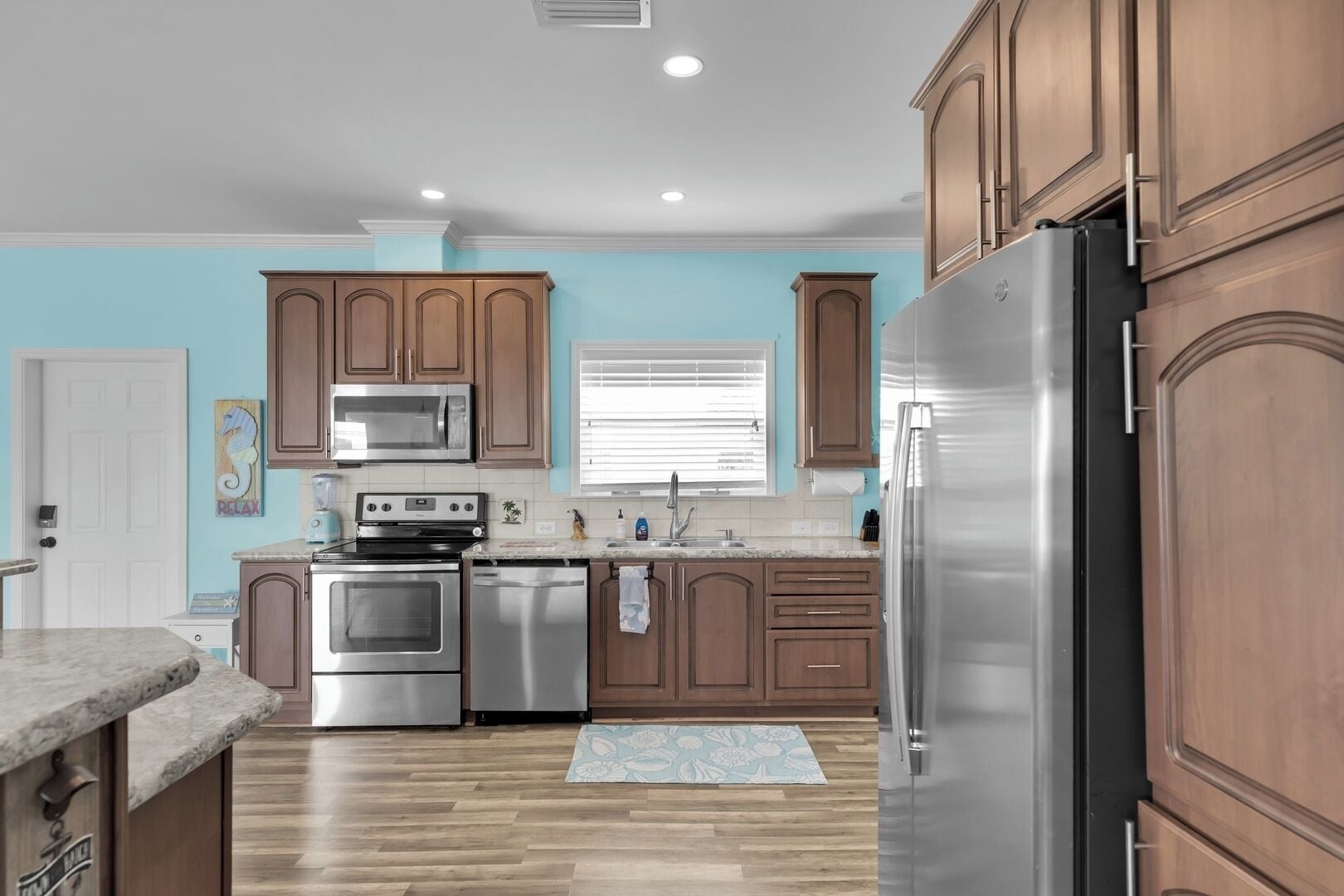A kitchen with wooden cabinets, stainless steel appliances, a marble countertop, and a patterned rug.