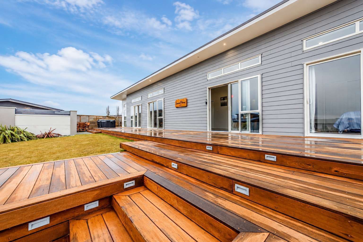 A modern house with a wooden deck, a large sliding glass door, and a sign that reads 'Home.'