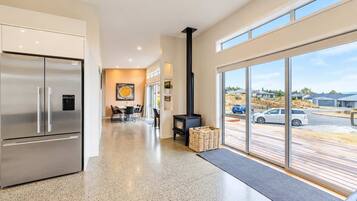 A modern kitchen with a stainless steel refrigerator, a dining area with a table and chairs, and a large window overlooking a parking area.