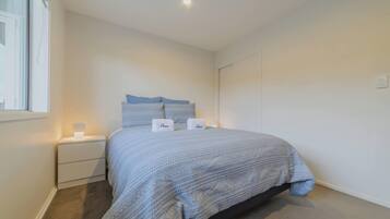 A bedroom with a bed, two pillows, a bedside table with a lamp, and a window.
