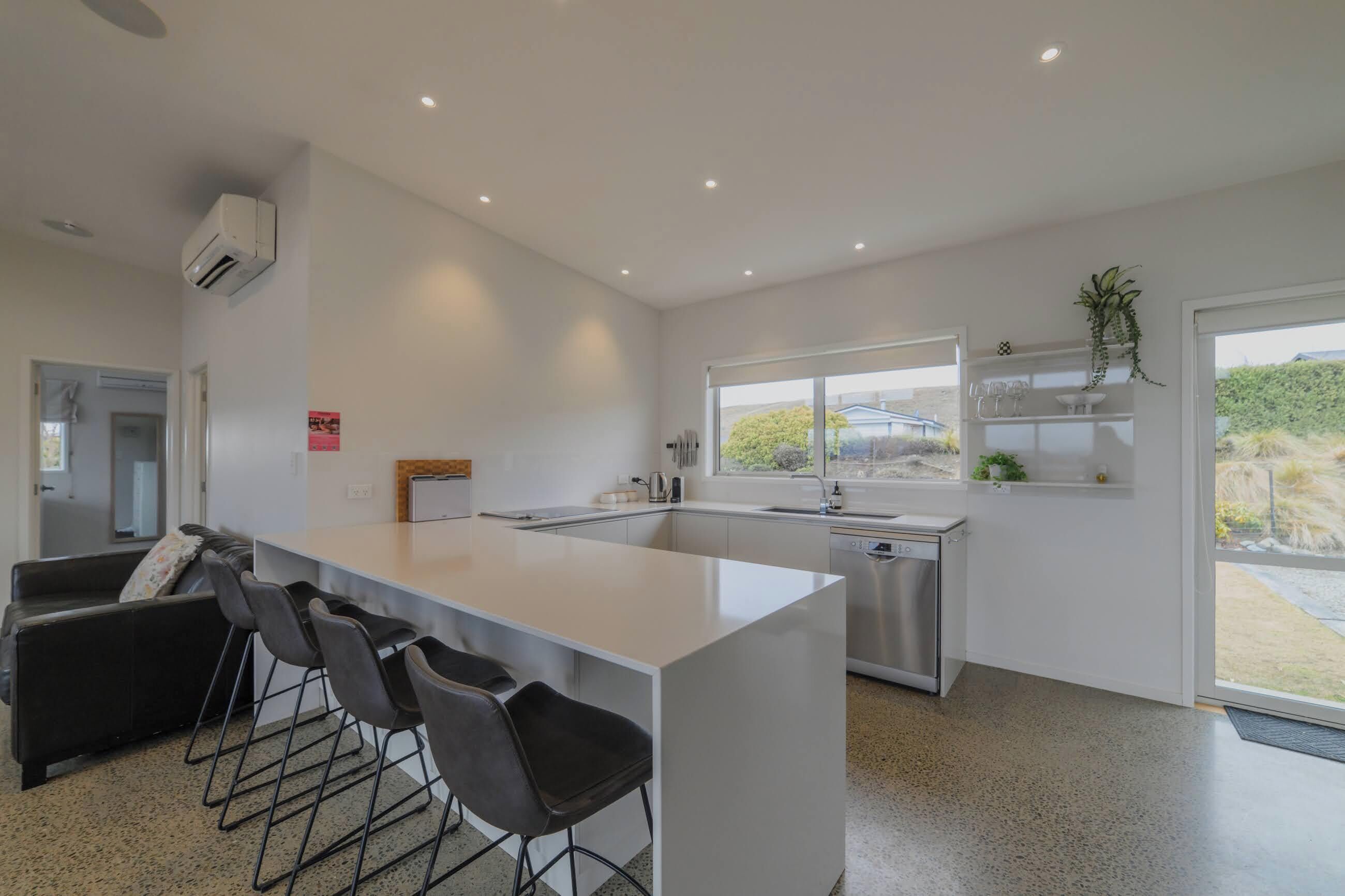 A modern kitchen with a central island, bar stools, a dishwasher, and a window with a view.