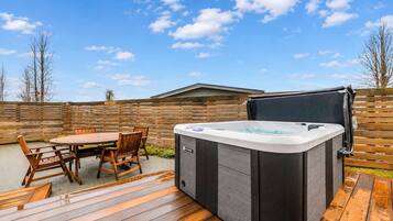 An outdoor patio with a hot tub, wooden deck, and a table with chairs.