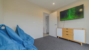 A room with a large flat-screen TV on the wall, a blue bean bag, a wooden cabinet, and a carpeted floor.