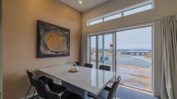 A modern dining area with a white table, black chairs, a glass enclosure, and a large window with curtains.