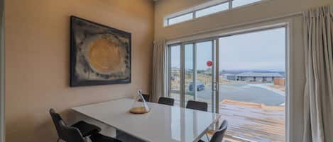 A modern dining area with a white table, black chairs, a glass enclosure, and a large window with curtains.