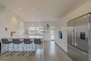 A modern kitchen with a stainless steel refrigerator, bar stools, and a large window.