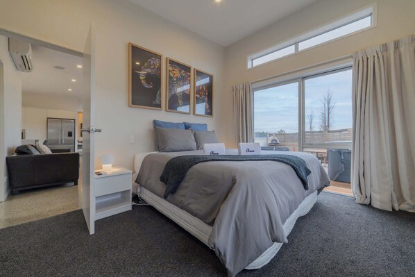 A modern bedroom with a large bed, a bedside table, a nightstand, a dresser, and a window with curtains.