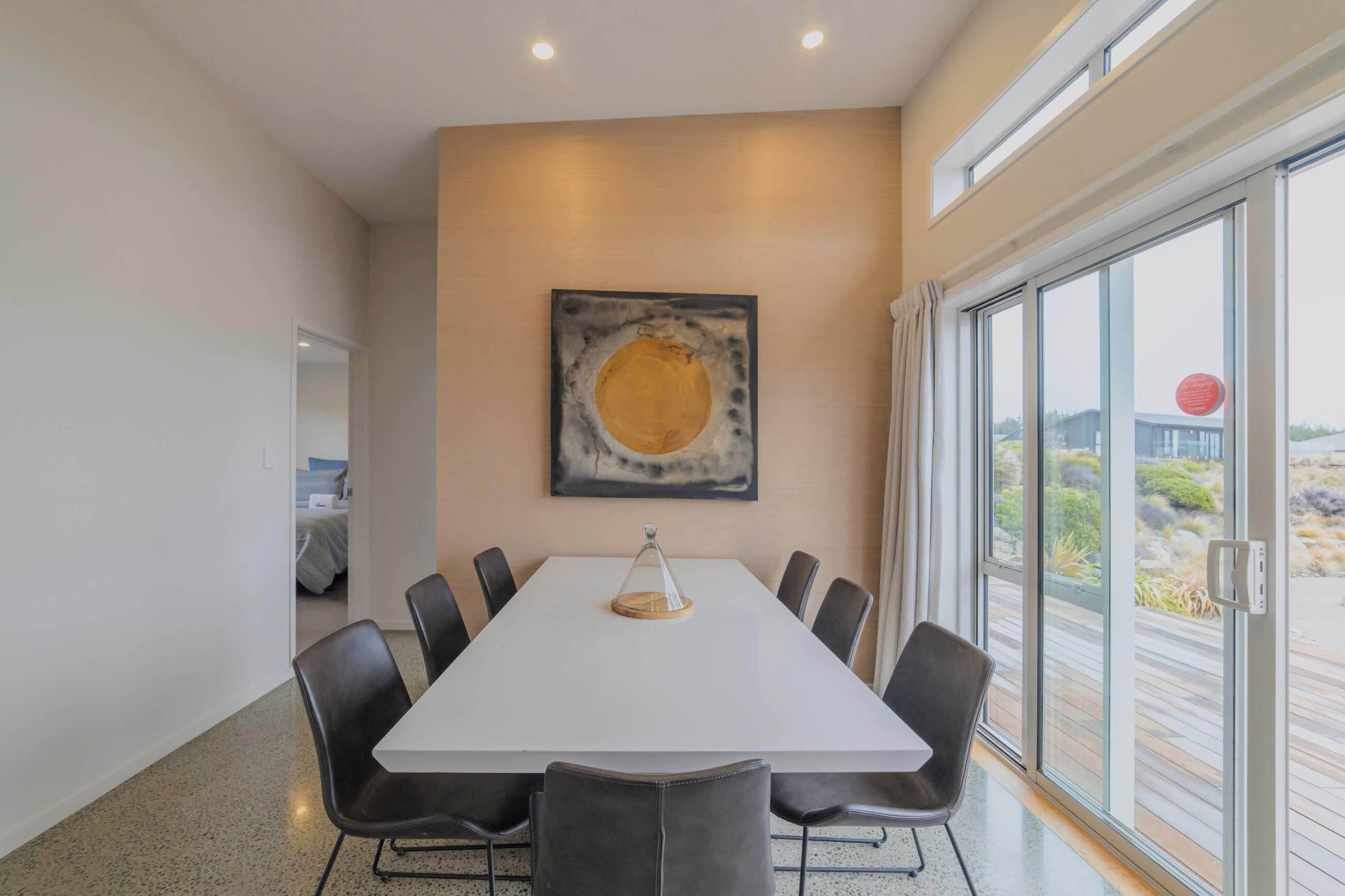 A conference room with a white table, black chairs, a large abstract painting, and a view of the outdoors through a glass door.