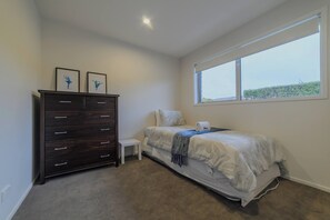 Une chambre à coucher avec un lit, une commode, une petite table et une fenêtre.