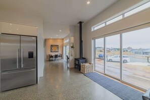 A modern kitchen with a stainless steel refrigerator, a dining area with a table and chairs, and a large window overlooking a parking area.