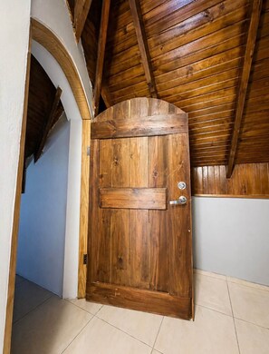 A wooden door with a metal handle and a keyhole, set in a hallway with a tiled floor and a wooden ceiling. - 87 Suites/ The Attic – Modern 1BR in West Village (Montego Bay)