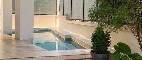 A modern outdoor pool area with a clear view of the pool, a potted plant, and a stone pathway leading to the pool.