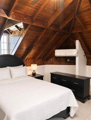 A bedroom with a sloped ceiling, a bed, bedside tables, a dresser, and an air conditioning unit. - 87 Suites/ The Attic – Modern 1BR in West Village (Montego Bay)