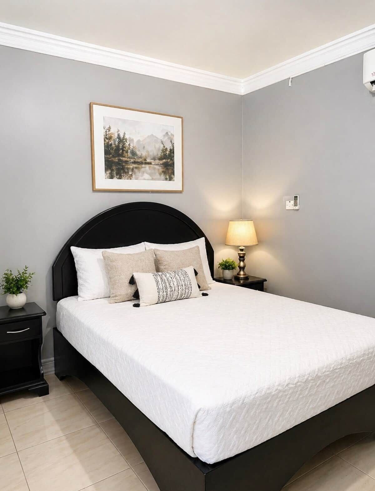 A bedroom with a bed, a nightstand, a lamp, a wall-mounted phone, and a framed picture.