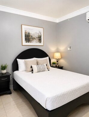 A bedroom with a bed, a nightstand, a lamp, a wall-mounted phone, and a framed picture. - 87 Suites | The Haven – Modern 1BR in West Village (Montego Bay)