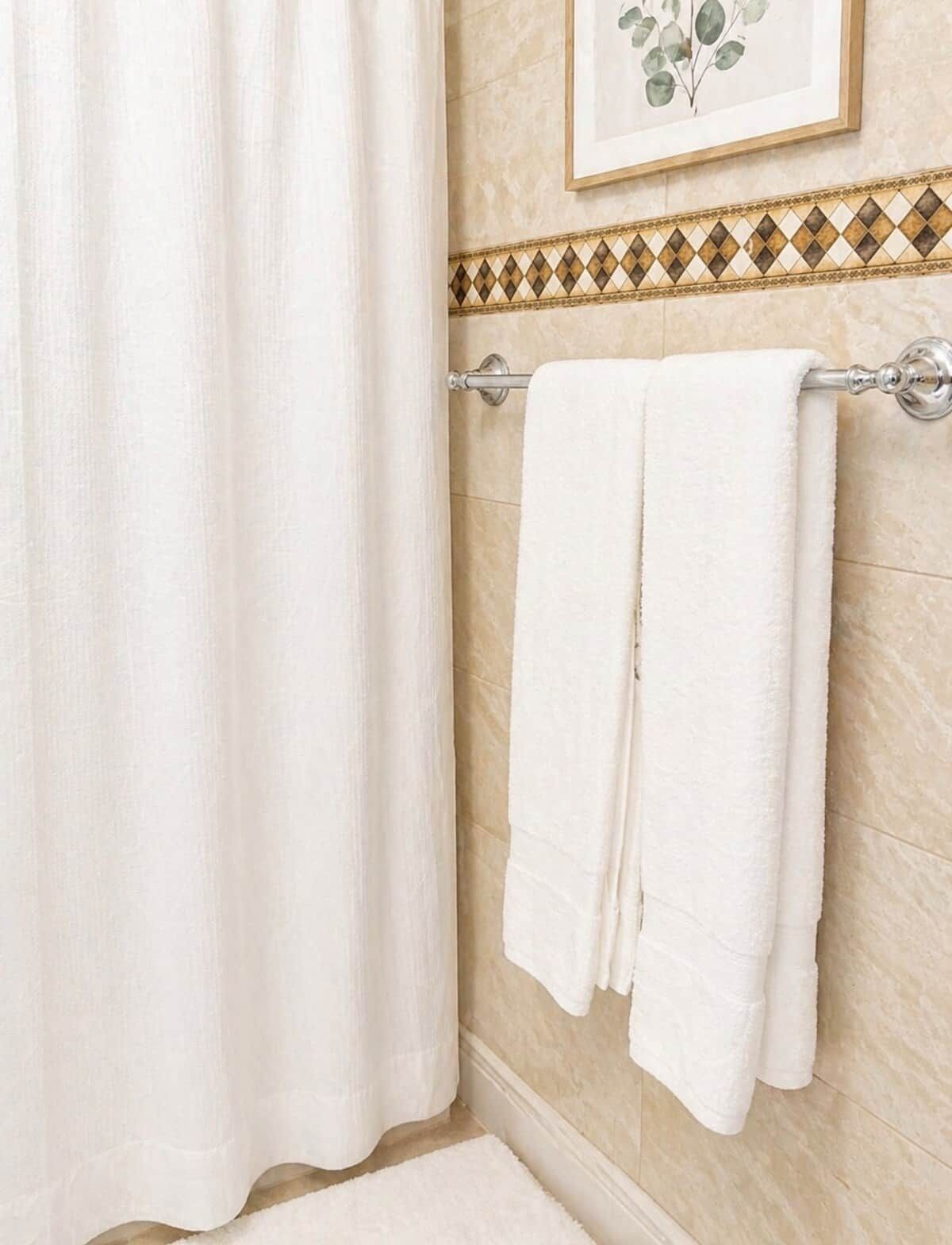 A bathroom with a shower curtain, a towel rack with two towels, and a framed botanical print on the wall.