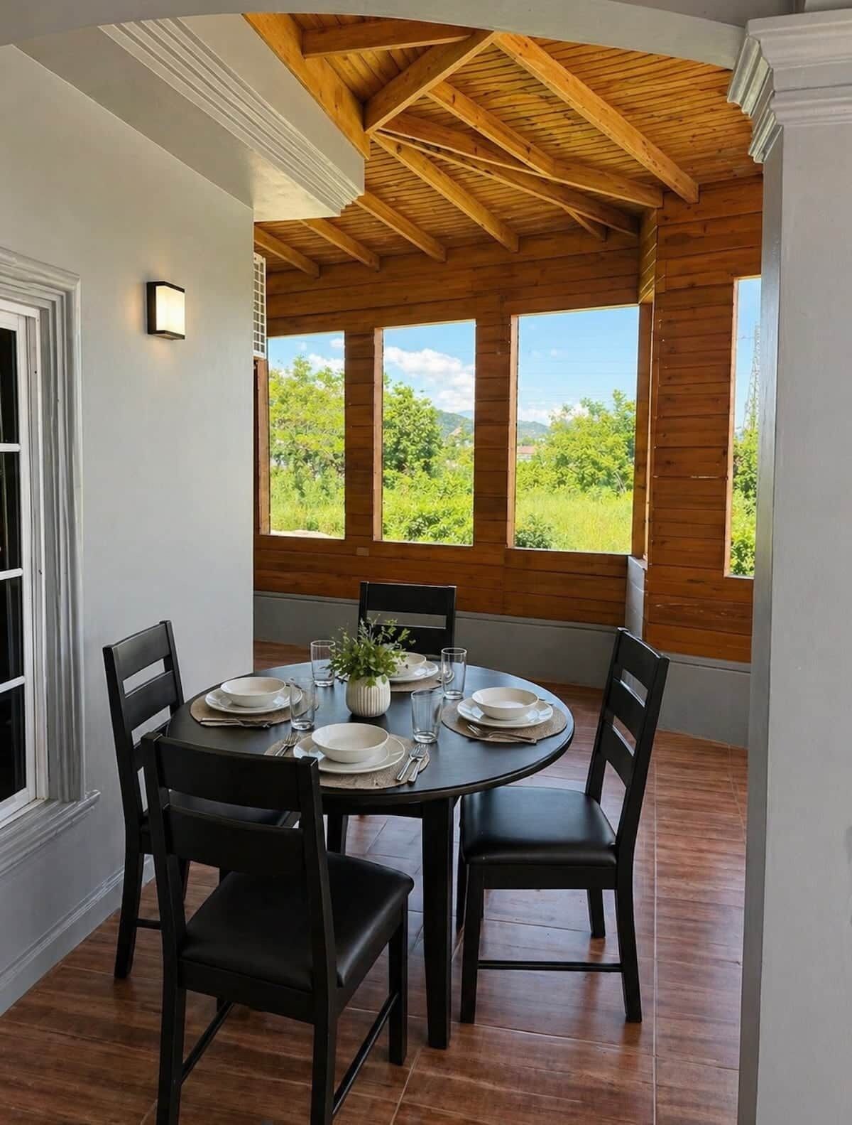 Un coin repas avec une table ronde, quatre chaises et une vue sur la verdure grâce à de grandes fenêtres.