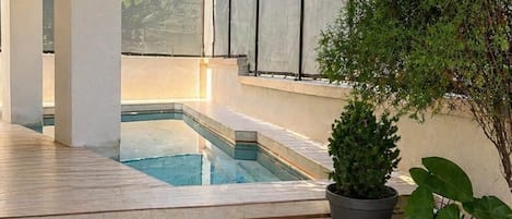 A modern outdoor pool area with a clear view of the pool, a potted plant, and a stone pathway leading to the pool.