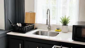 A kitchen with black cabinets, a stainless steel sink, a gas stove, and a window with sheer curtains.