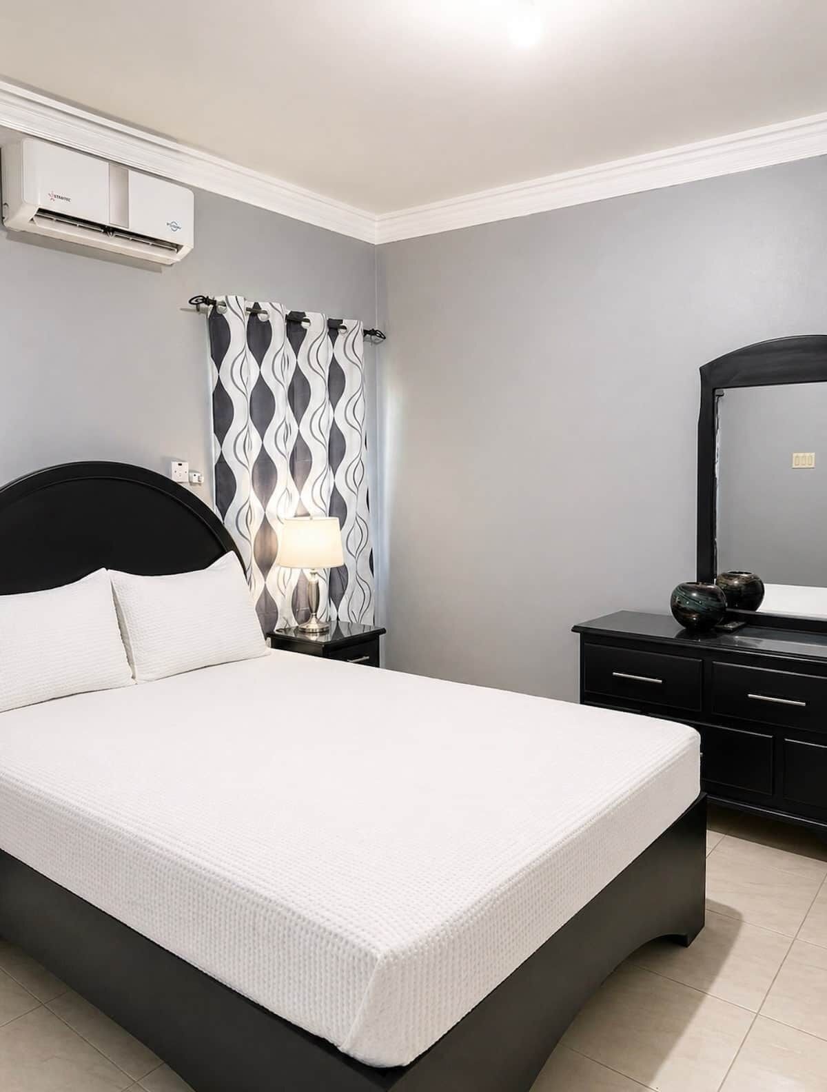 Un dormitorio con cama, lámpara de noche, cómoda y espejo.