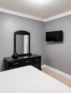 A bedroom with a bed, a dresser, a mirror, and a TV mounted on the wall. - 87 Suites | The Breeze– Modern 1BR W/Pool (Montego Bay)