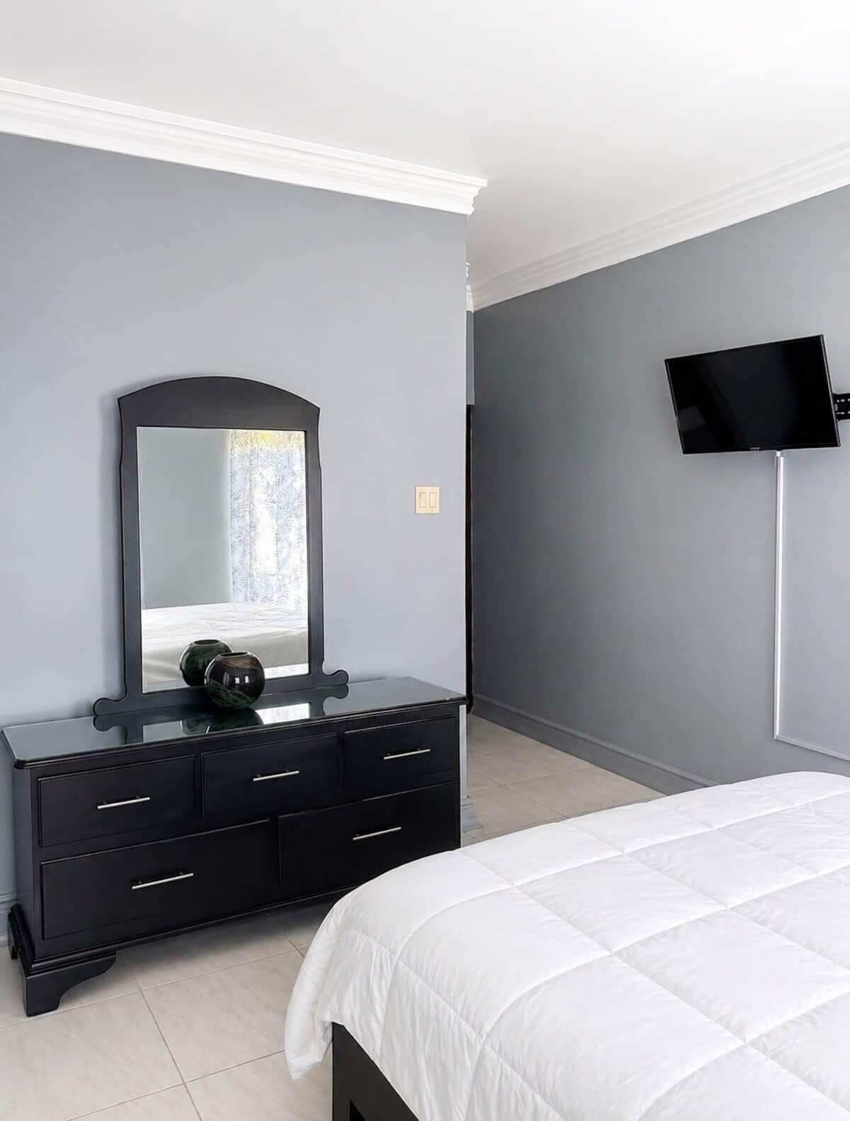 A bedroom with a bed, a dresser, a mirror, and a TV mounted on the wall.